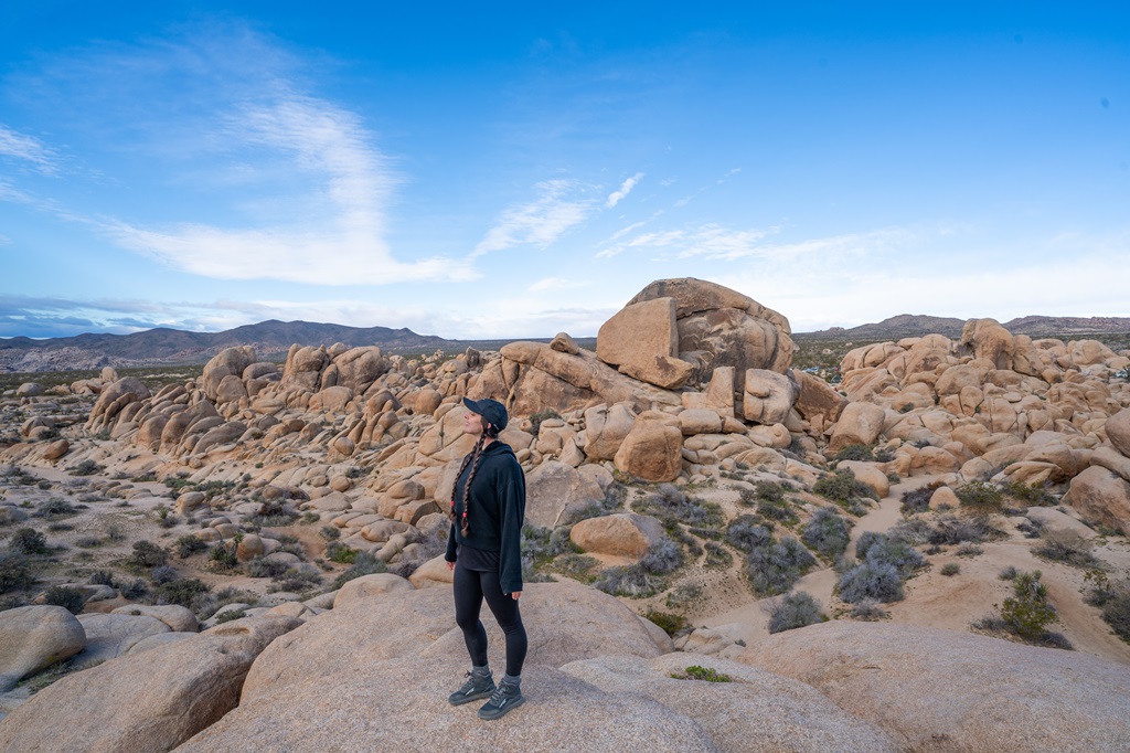 Woman standing in front of a boulder field near the Arch Rock Trail in Joshua Tree National Park.