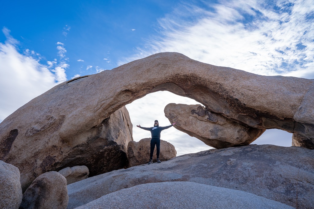 Man standing under Arch Rock in Joshua Tree National Park.