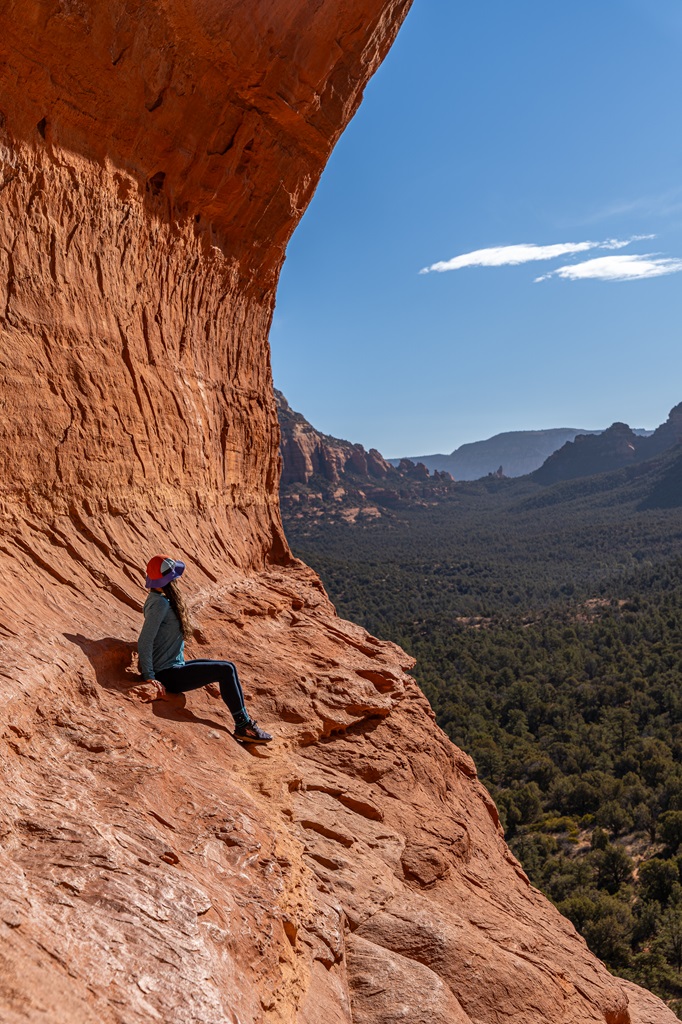 Woman sitting on a narrow ledge in the Birthing Cave after sunrise in Sedona.