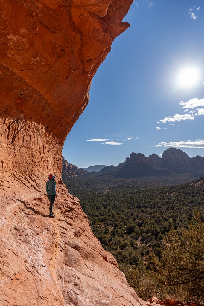 Woman standing on a narrow rocky ledge on the side of the Birthing Cave in Sedona.