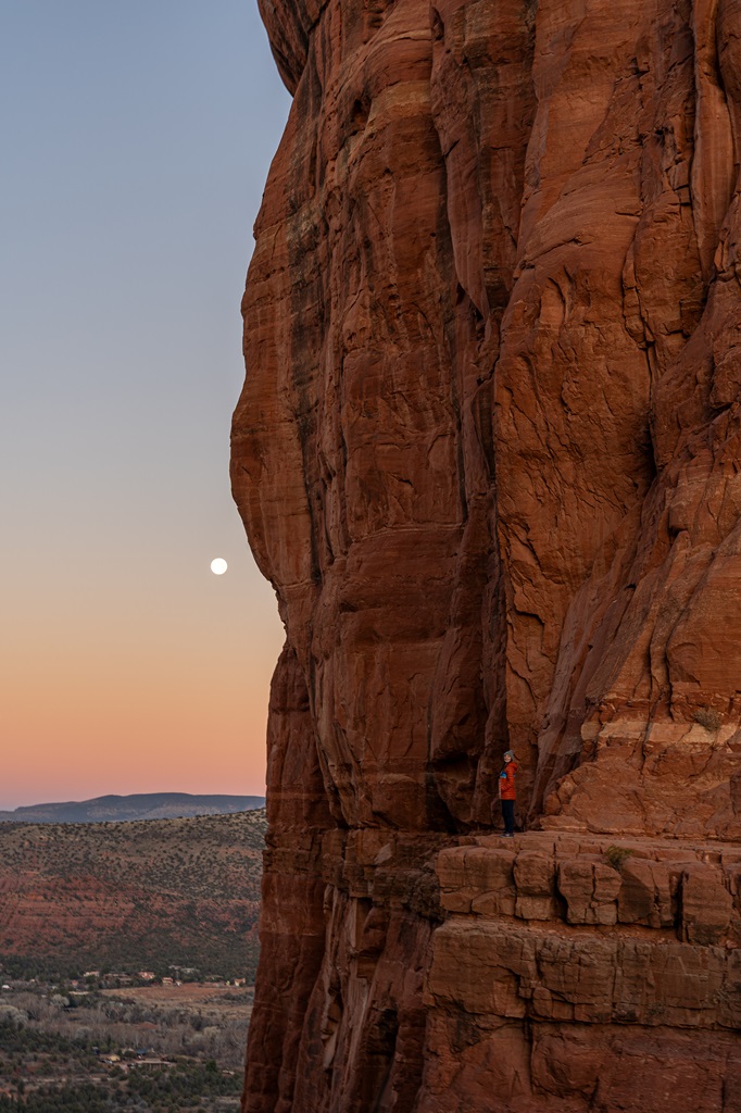 Woman standing on a rocky ledge at Cathedral Rock in Sedona during sunrise.