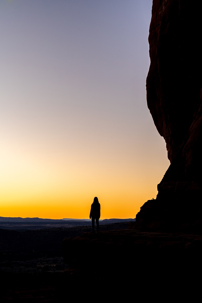 Woman standing on a rocky ledge at Cathedral Rock in Sedona during sunset.