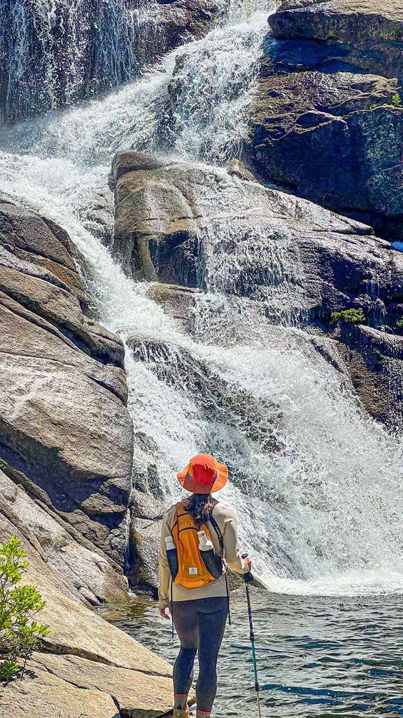 Woman standing in front of the upper portion of Chilnualna Falls in Yosemite National Park.