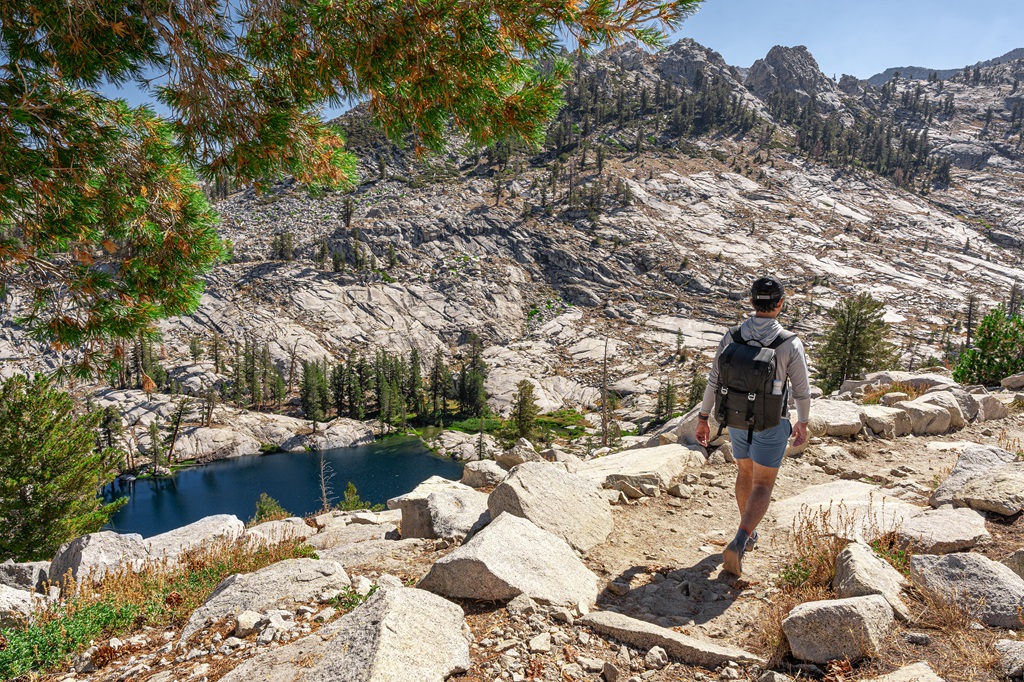 Man hiking along the Lakes Trail with a view of Aster Lake to the left.