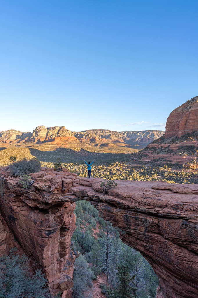 Woman standing on Devil's Bridge in Sedona with hands in the air.