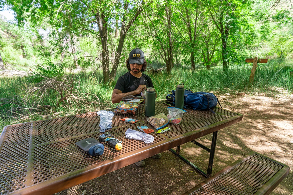 Man sitting at a picnic table with water and snacks set up at Havasupai Gardens.