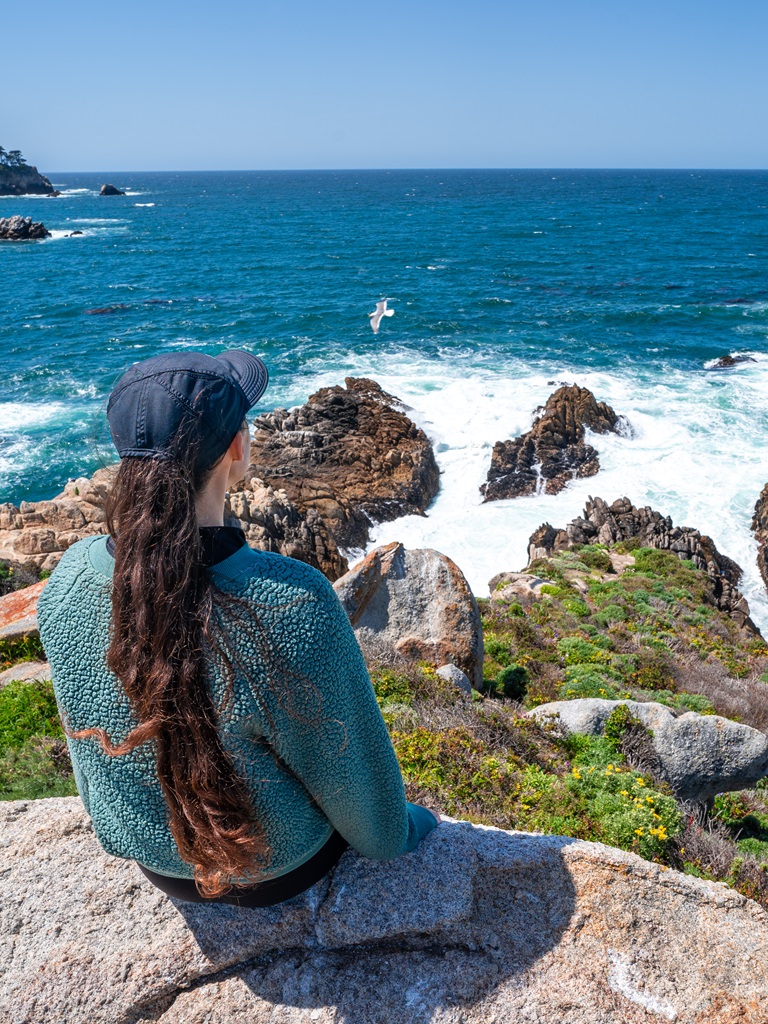 Woman sitting on the rocks overlooking the Pacific Ocean at Granite Point.