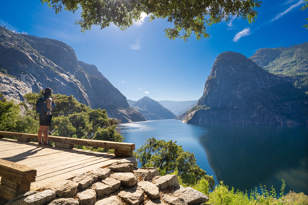 Man standing along a trail in Hetch Hetchy with views of the reservoir and granite peaks.