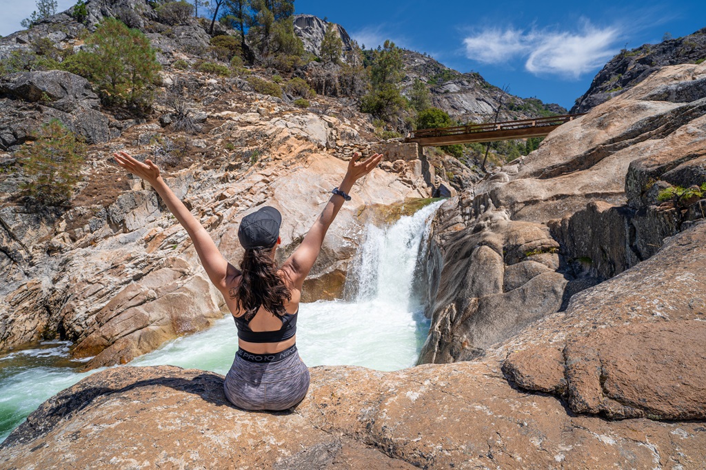 Woman sitting on rock with hands in the air in front of Rancheria Falls.