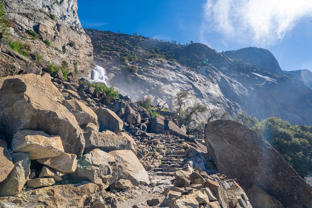 Man standing on the trail near Wapama Falls with hands in the air.