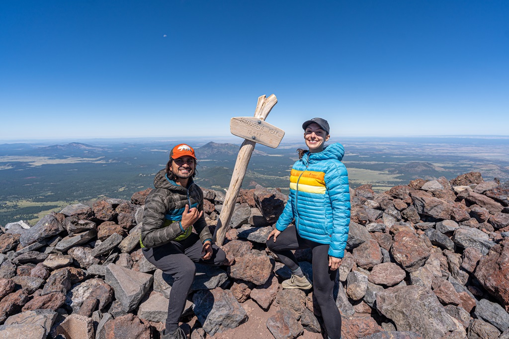 Man and woman posing beside the summit sign of Humphreys Peak.