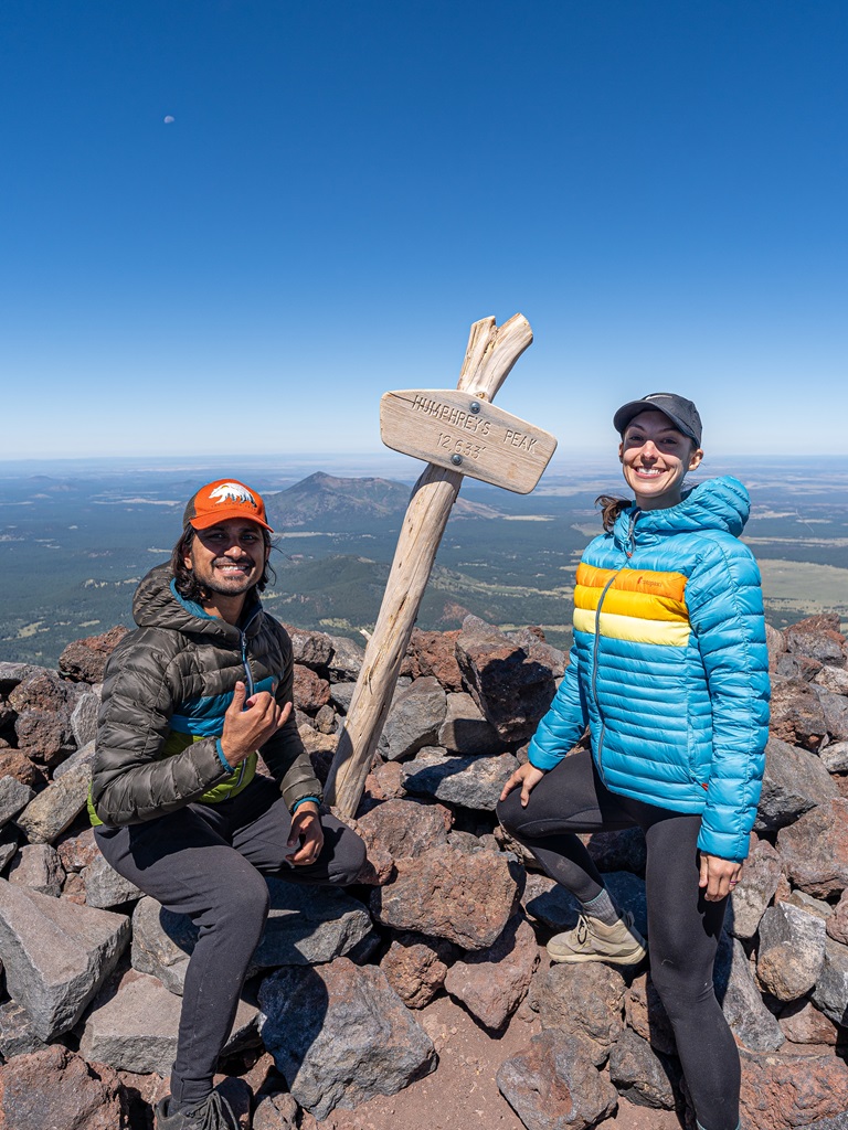 Man and woman posing beside the summit sign of Humphreys Peak.