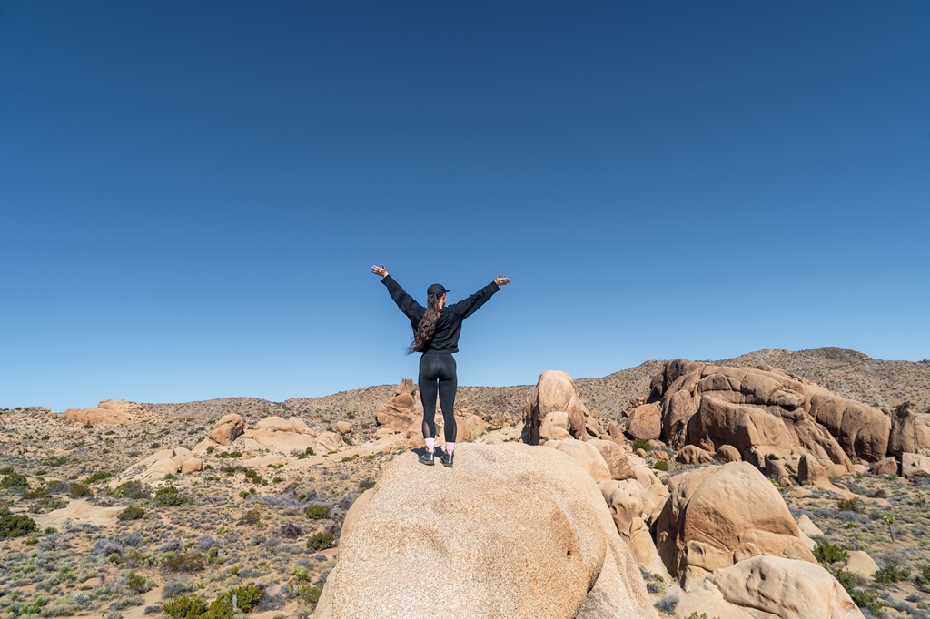 Woman standing on a big boulder with hands in the air in Joshua Tree National Park.