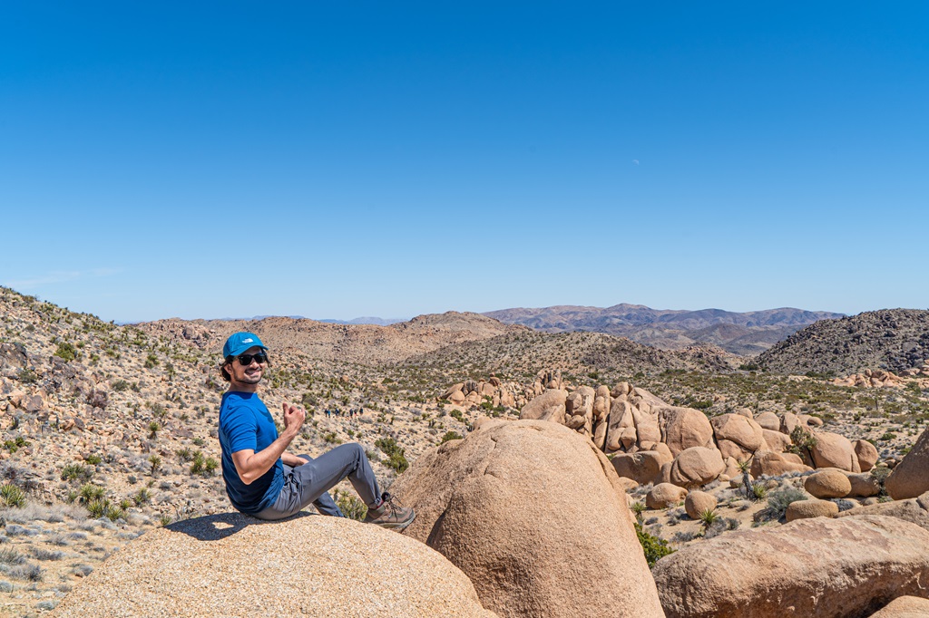 Man sitting on a boulder with views of Joshua Tree's desert landscape in the background.