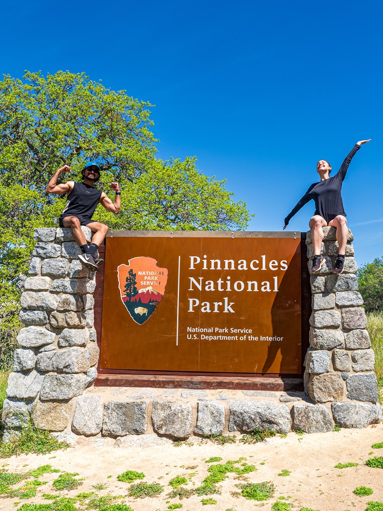 Man and woman sitting on the Pinnacles National Park sign.