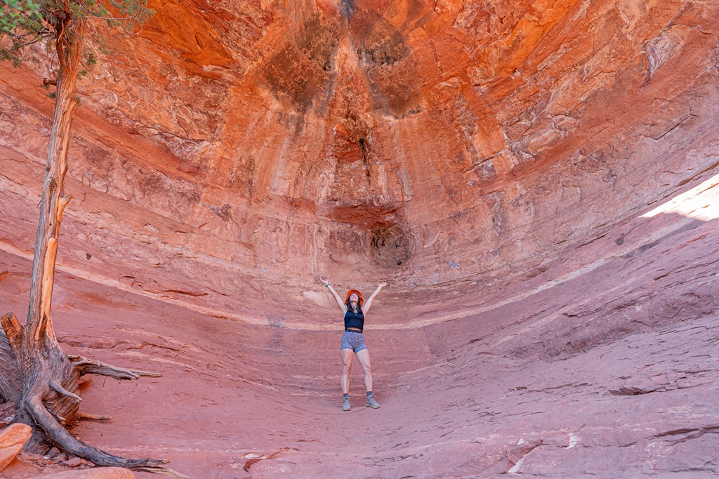 Woman standing inside the Birthing Cave and posing with hands in the air.