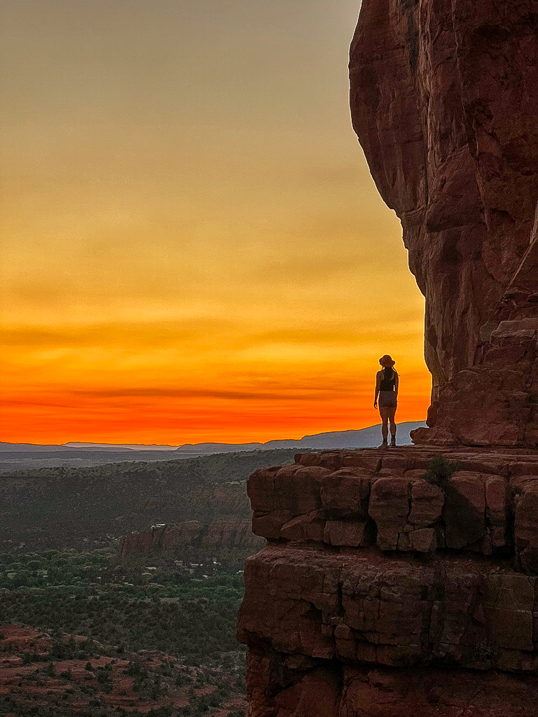 Woman standing on a ledge at Cathedral Rock during sunset.