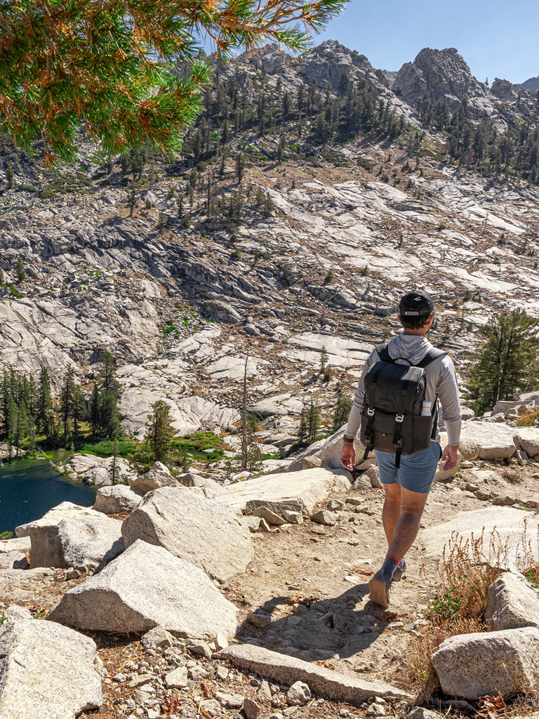 Man hiking along the Lakes Trail with a view of Aster Lake to the left.