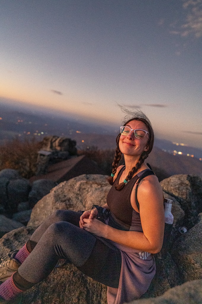 Woman sitting on a rock on the summit of Sharp Top watching the sunrise.