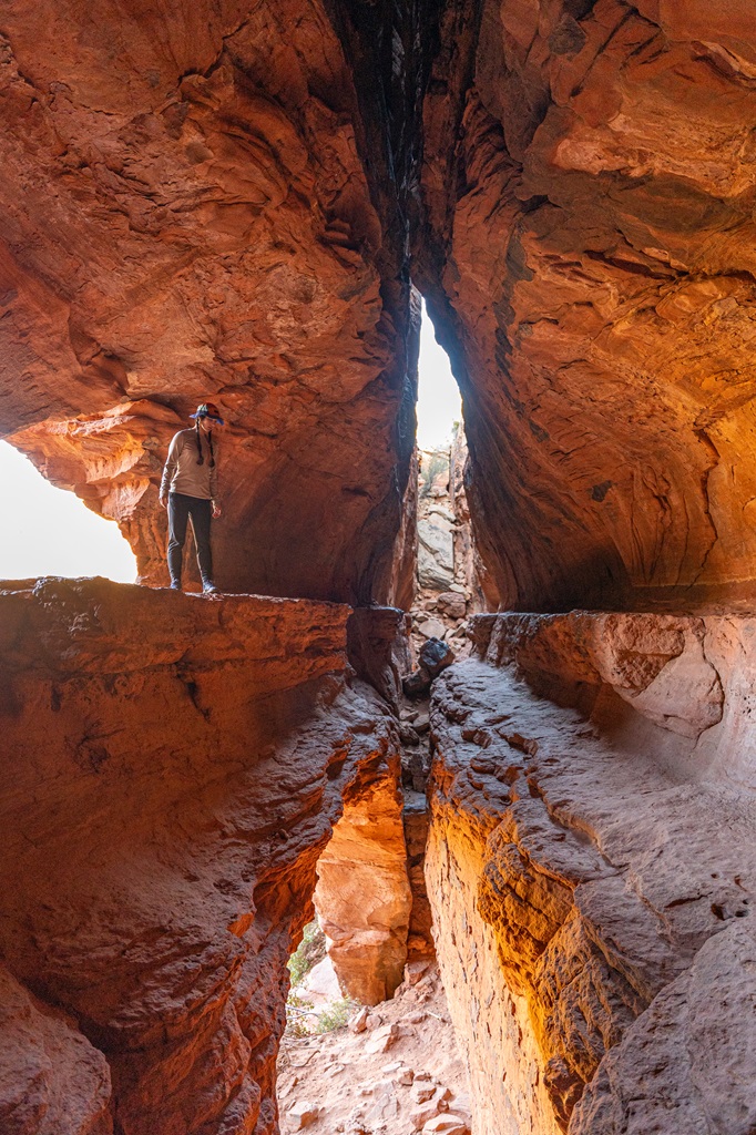 Woman standing on a rocky ledge looking down inside the Soldier Pass Cave in Sedona.