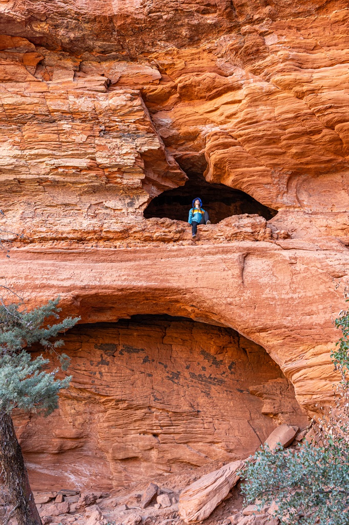 View of the outside of the Soldier Pass Cave in Sedona with a woman sitting safely on a rocky ledge.