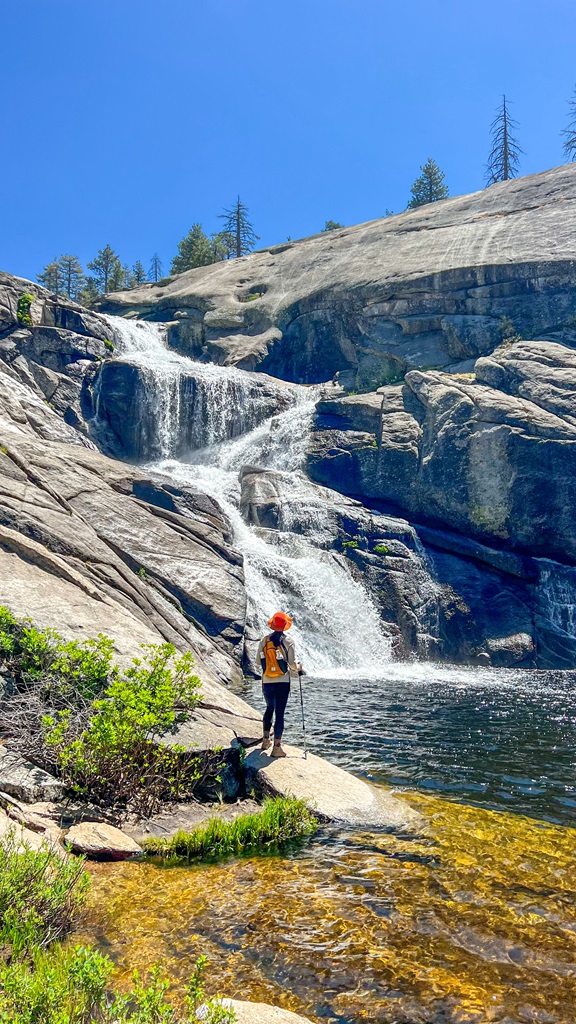 Woman standing on a rock near the upper portion of Chilnualna Falls in Yosemite National Park.