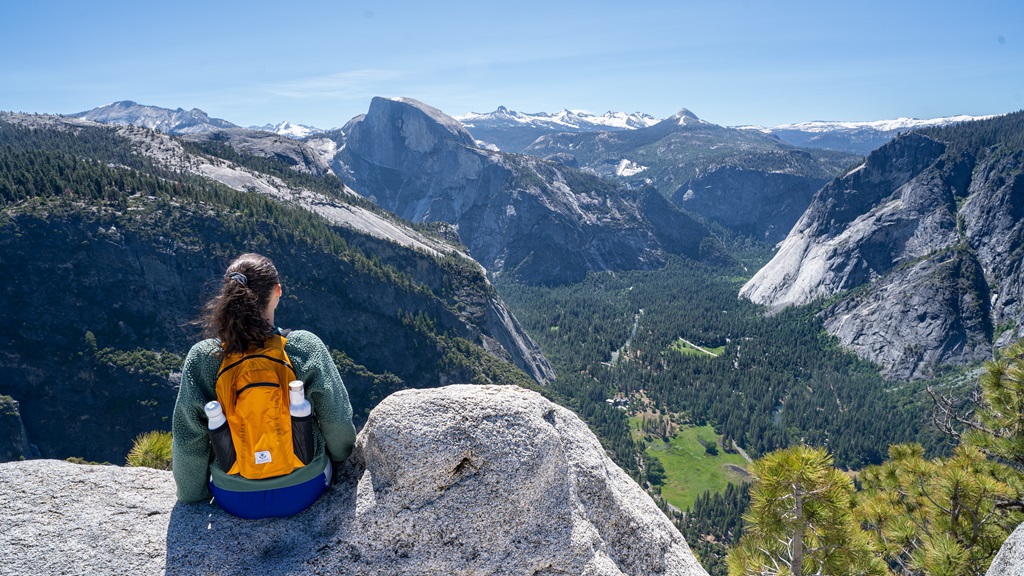 Woman sitting on a rock at Yosemite Point looking at the jaw-dropping views of Half Dome and snowy mountains.