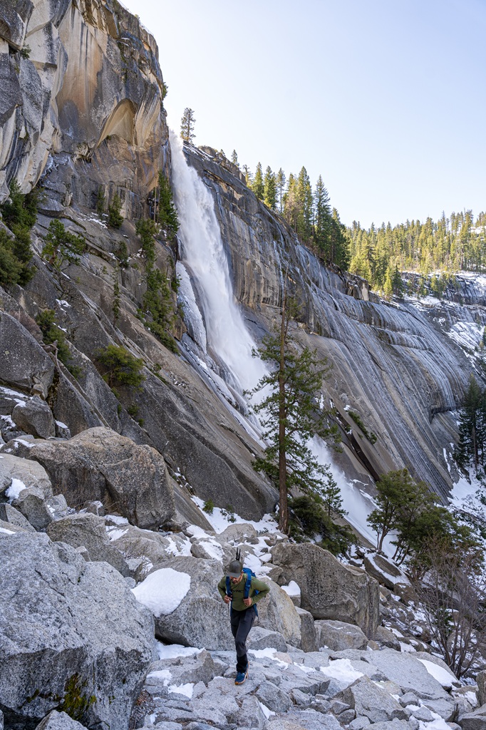 Man hiking the Mist Trail to the top of Nevada Fall with snow patches all around in Yosemite National Park.