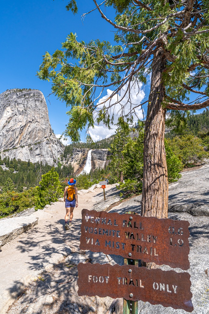 Woman hiking on the Clark Point cutoff trail with Liberty Cap and Nevada Fall in the distance.