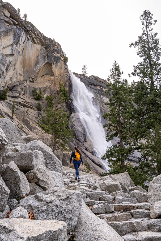 Woman hiking a rocky section on the Mist Trail with Nevada Fall nearby in Yosemite National Park.