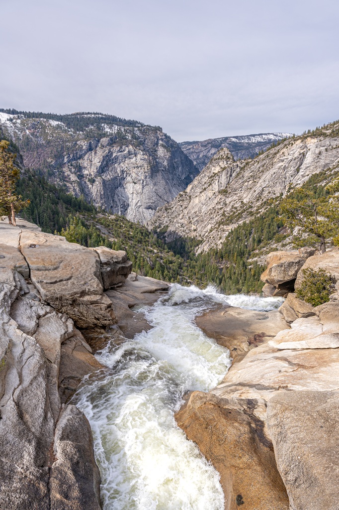 View from the footbridge of the river running over the cliff to form Nevada Fall and granite peaks in the distance.