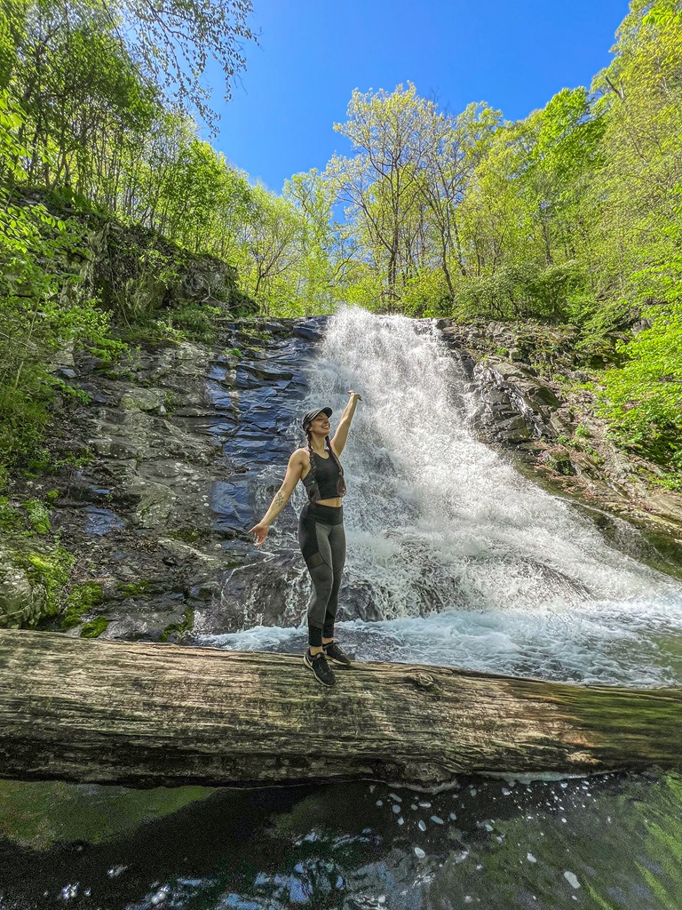 Woman standing on a fallen tree in front of Whiteoak Canyon Falls #5 located in Shenandoah National Park.