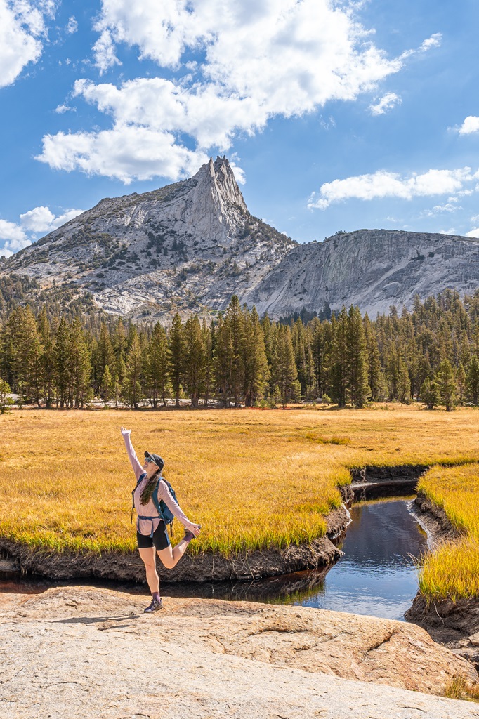 Woman posing in front of a meadow and Cathedral Peak near Lower Cathedral Lake in Yosemite.