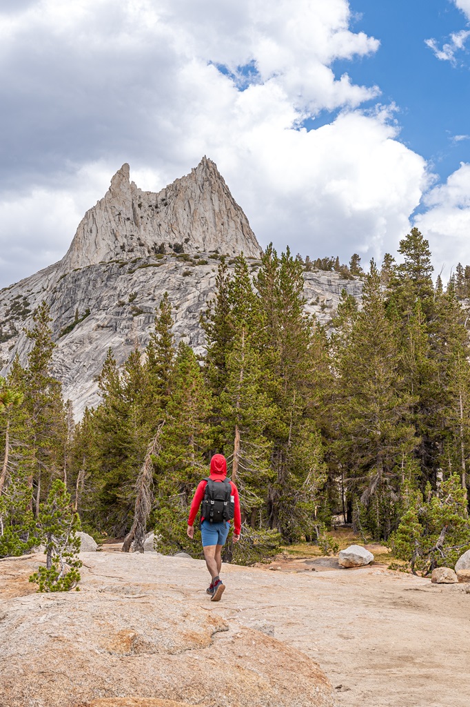 Man hiking along the John Muir Trail near Upper Cathedral Lake with Cathedral Peak in the background.