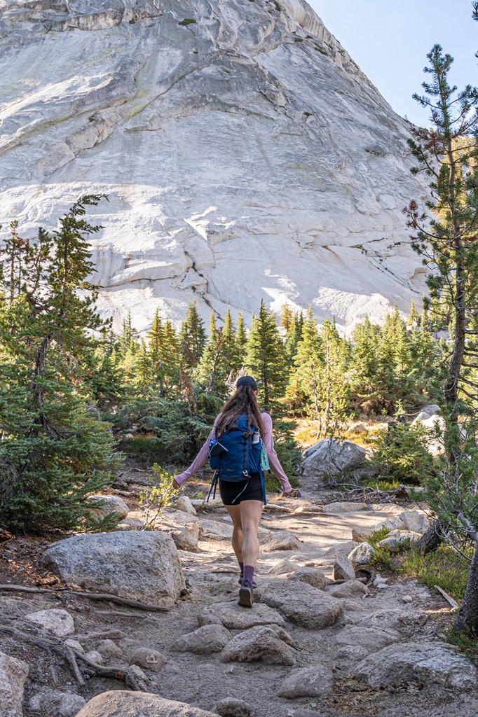 Woman hiking along the John Muir Trail in Yosemite with the north shoulder of Cathedral Peak in the background.