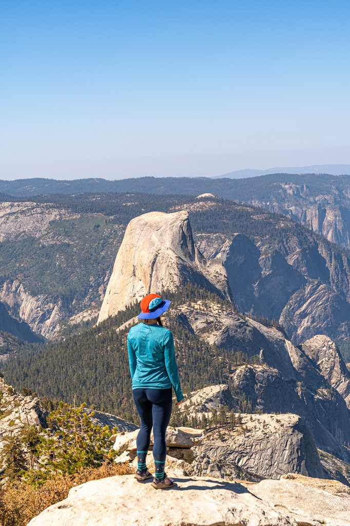 Woman standing on Clouds Rest with Half Dome in the background.