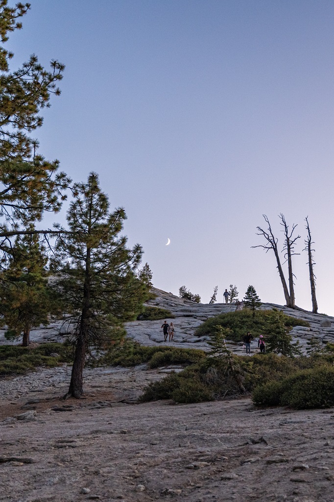 People descending Sentinel Dome after watching sunset with a crescent moon in the sky.