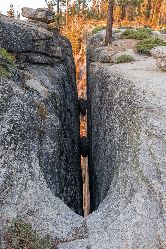 Deep crack in the granite known as a fissure with two small rocks jammed in between the fissure.