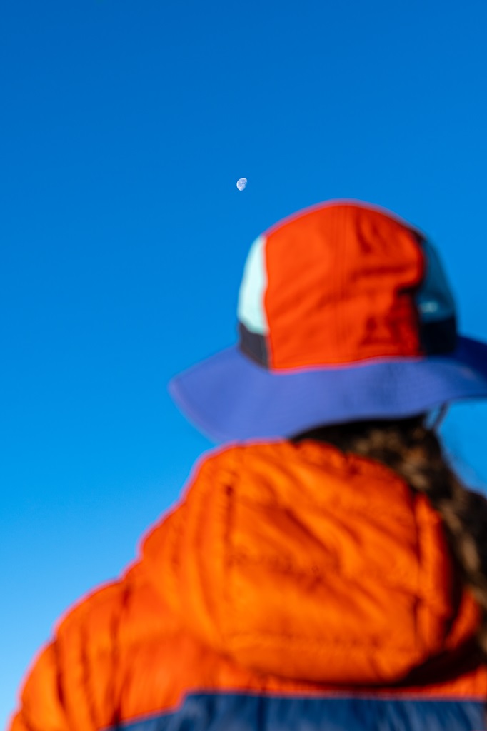 Close-up, blurry view of woman wearing down jacket and bucket hat with a clear view of the moon.