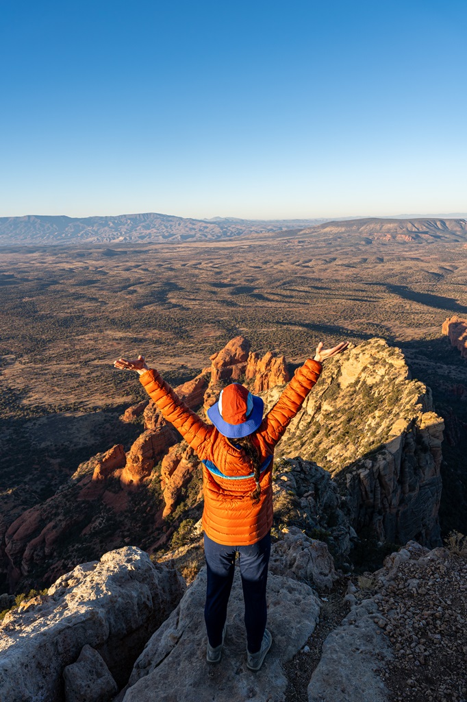 Woman standing on the summit of Bear Mountain in Sedona with hands in the air celebrating making it to the top.