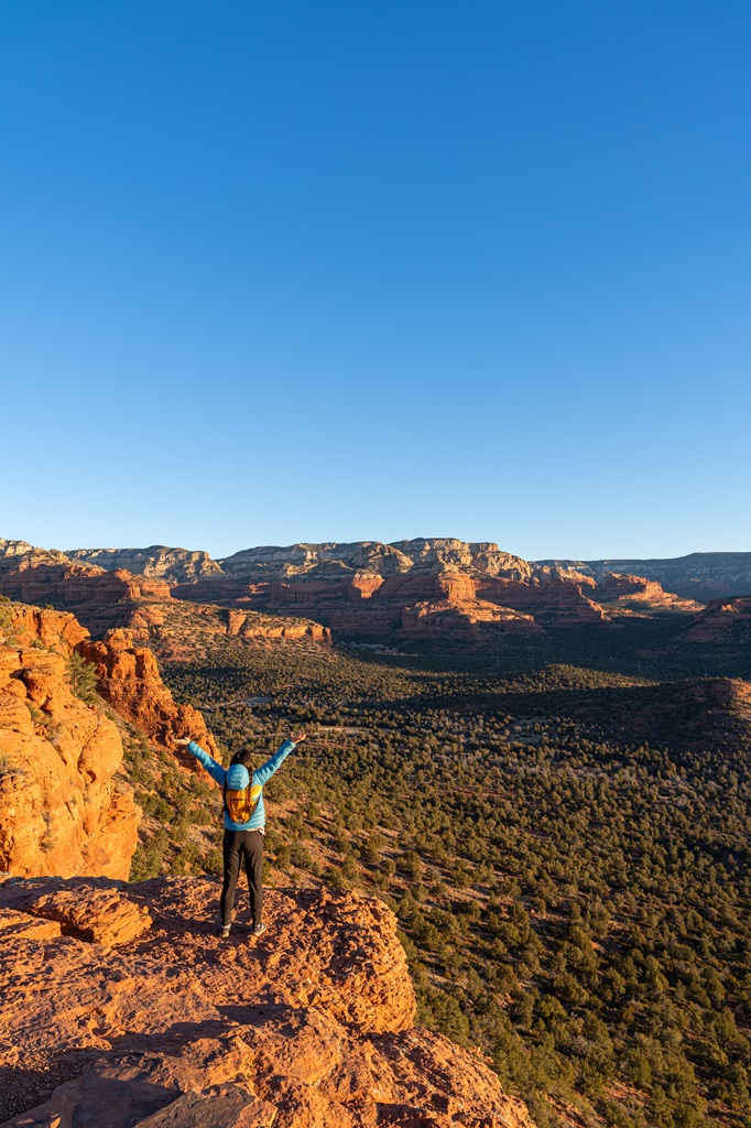 Woman standing on a rocky outcrop on Doe Mountain in Sedona with hands in the air.