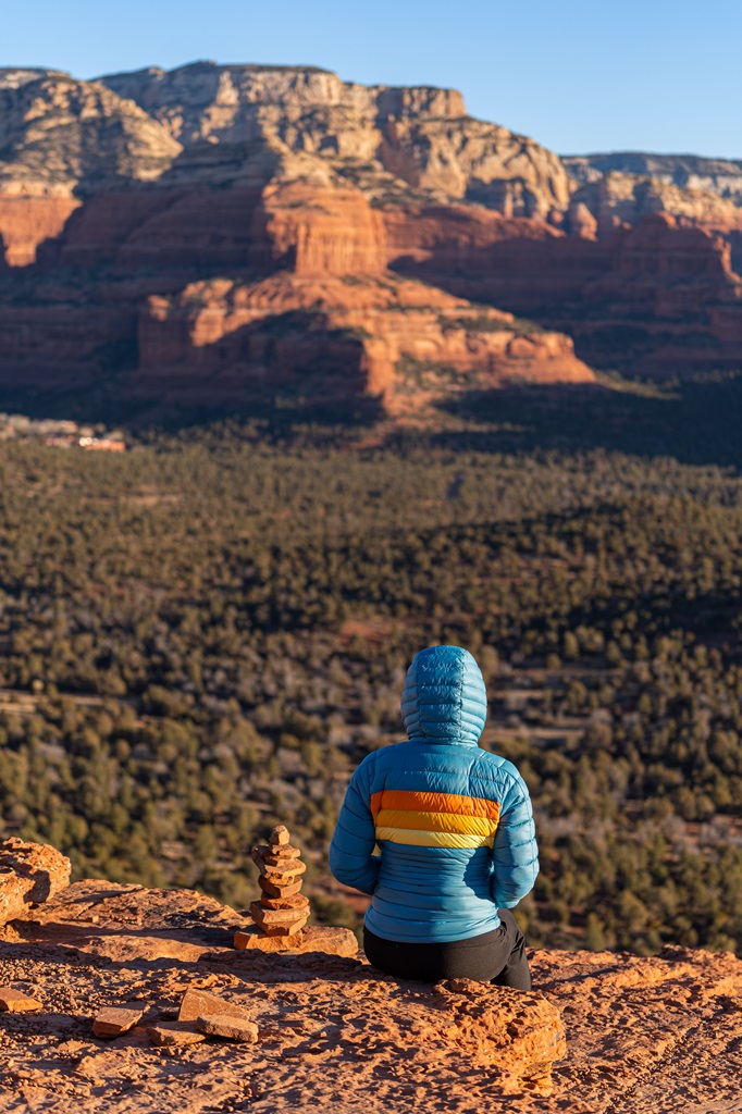 Woman sitting beside a cairn on a rocky outcrop on Doe Mountain in Sedona.