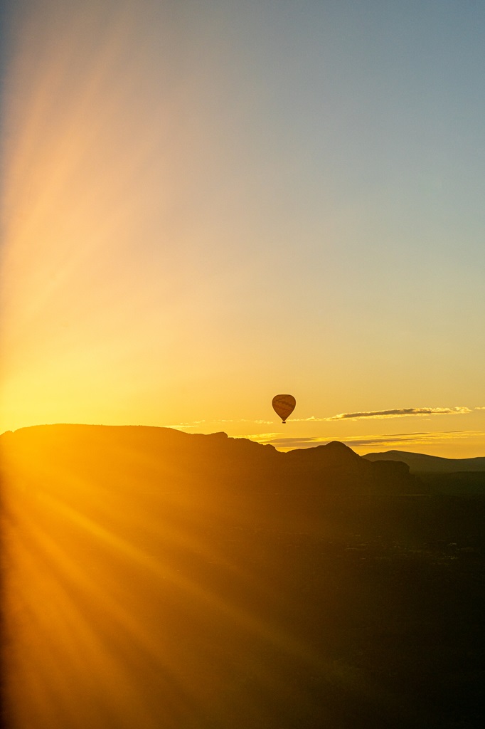 Hot air balloon floating through the sky with bright sunrise glare.