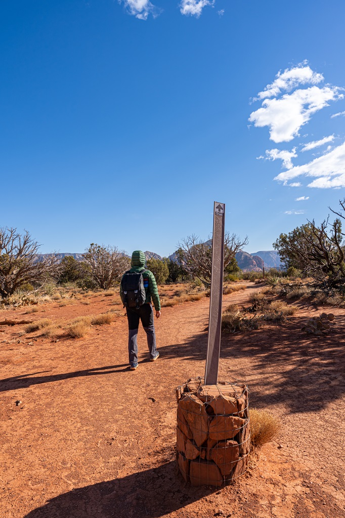 Man hiking along a trail in Sedona and a trail sign pointing towards the end of the Doe Mountain Trail.