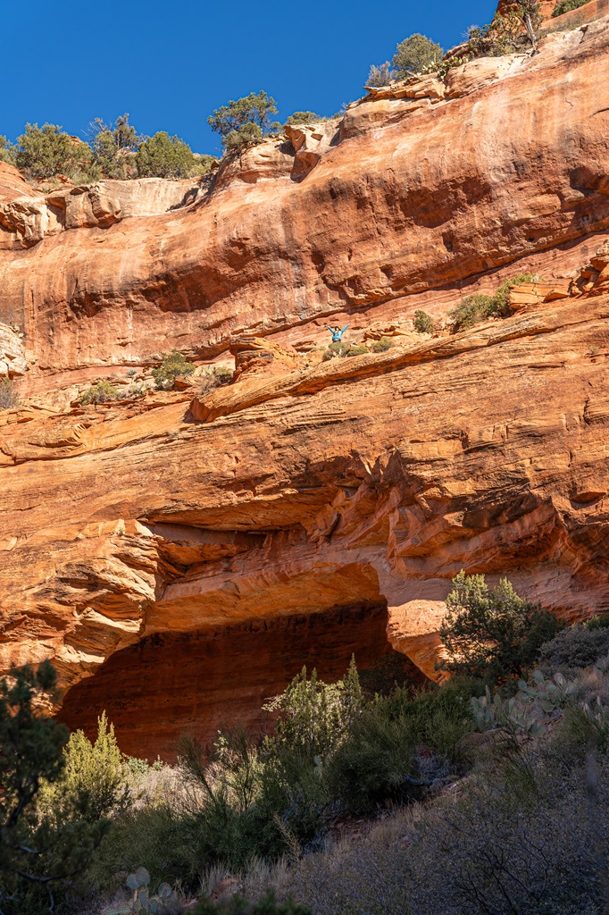 Woman standing on top of Fay Canyon Arch with hands in the air.