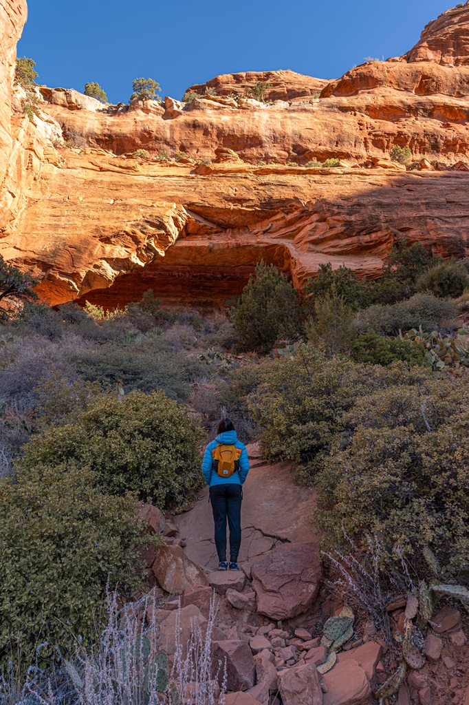 Woman standing on a social trail looking up at Fay Canyon Arch in Sedona.