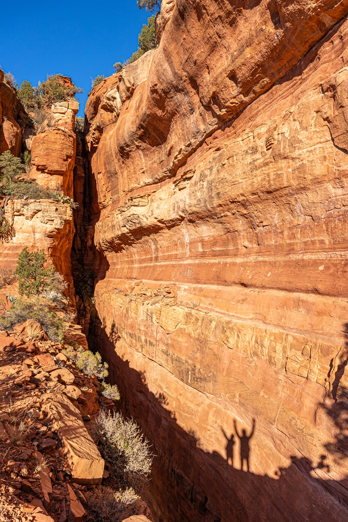 Shadow of man and woman on the red sandstone wall celebrating making it to the top of Fay Canyon Arch in Sedona.