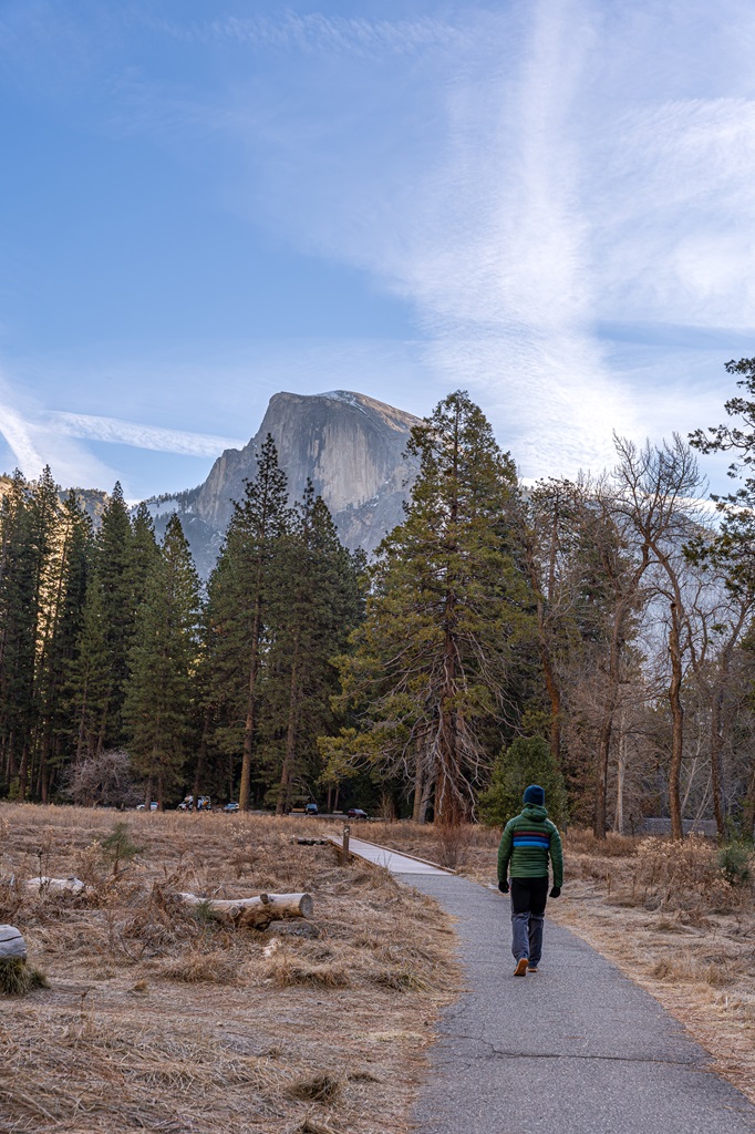 Man walking along the Cook's Meadow loop trail with Half Dome in the background.