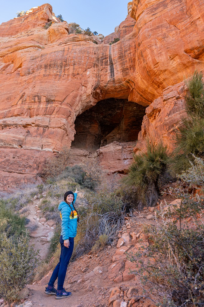 Woman standing about 0.1 miles away from the base of Keyhole Cave and pointing towards the opening.