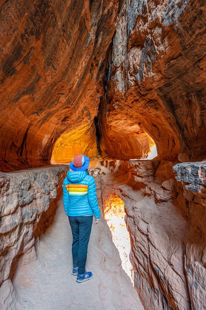 Woman standing in the Soldier Pass Cave with the early morning light illuminating the inside of the cave in a bright orange color.